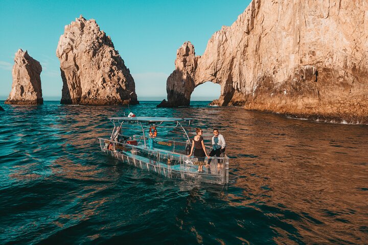 Clear-hulled boat beside a sea arch
