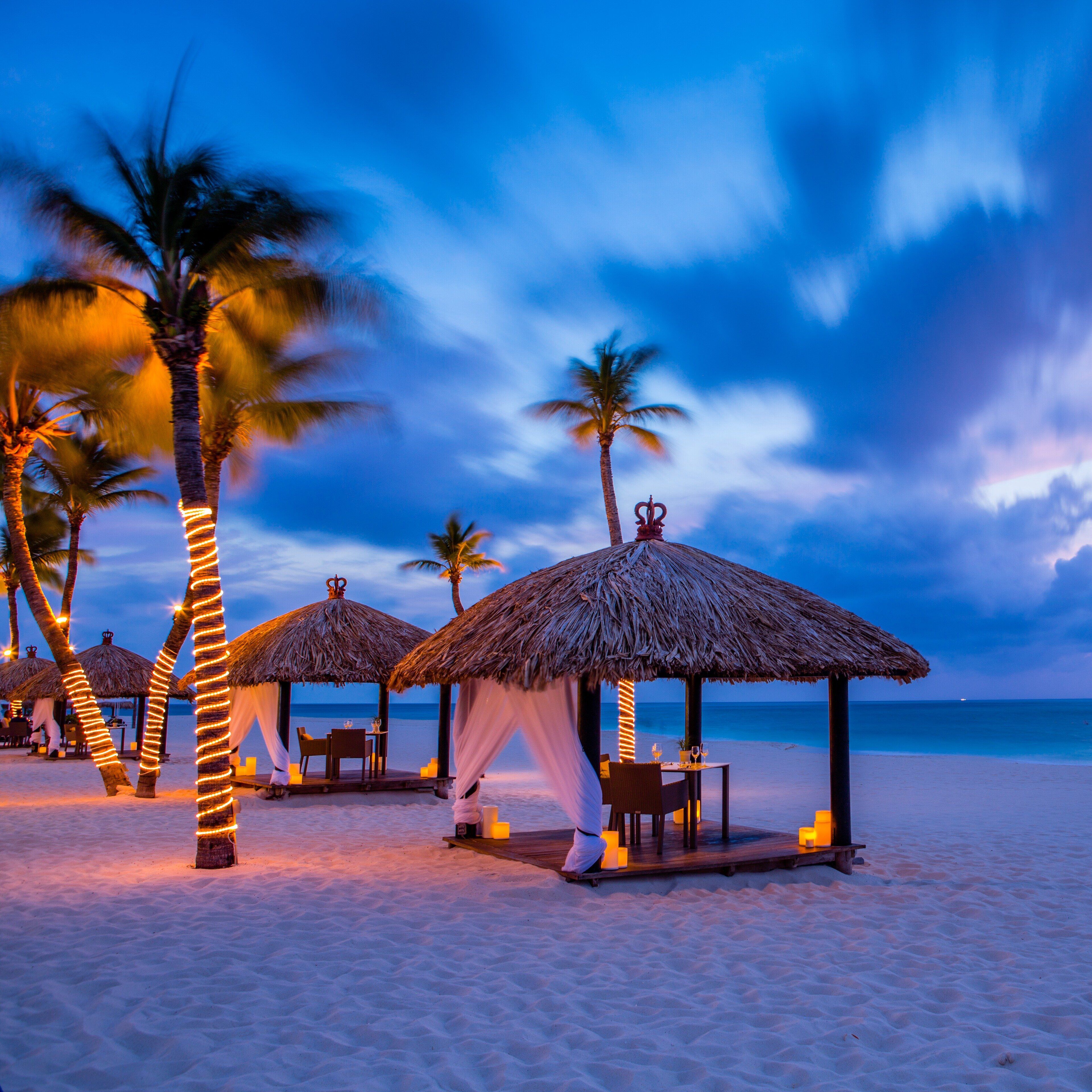 Lit cabanas on the sand at dusk